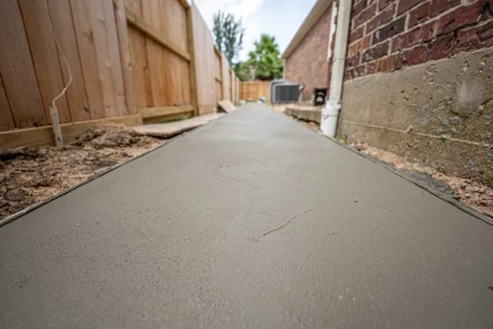 Freshly poured concrete path between a wooden fence and brick wall in a narrow alley