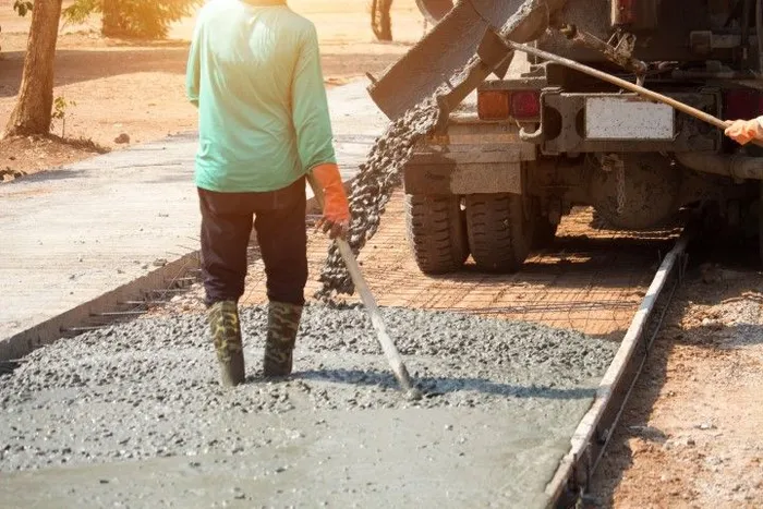 Worker leveling wet concrete beside a road construction truck