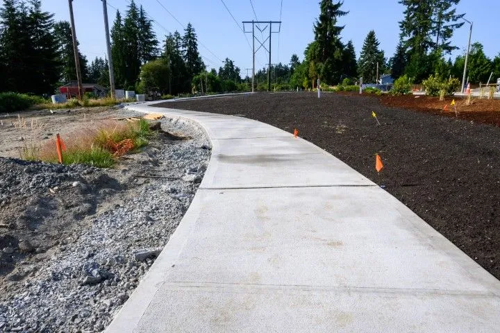 Curved concrete walkway beside gravel and fresh landscaping under tall power lines